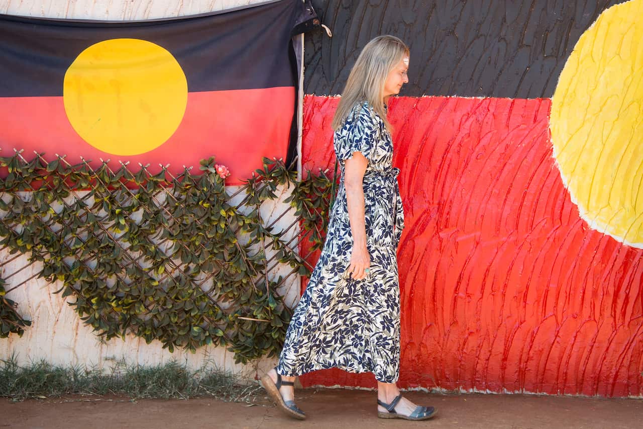 A woman in a blue floral dress walking along a wall with the Aboriginal flag draped along it - red, black and yellow