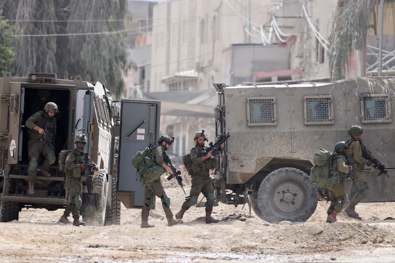A group of soldiers in uniforms with guns emerge from armoured vehicles.