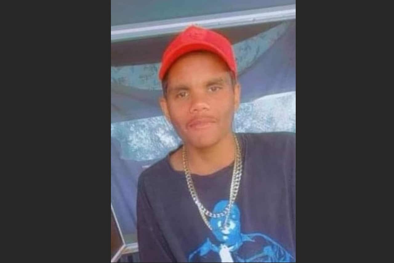 A man wearing a black t-shirt, red cap, and a necklace.