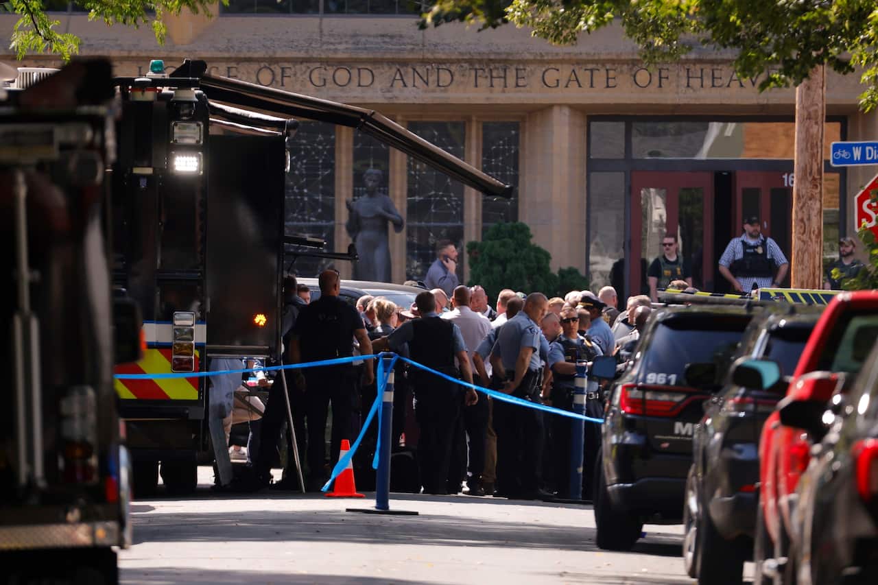 A crowd gathered outside a church after a shooting incident. There's a row of vehicles in the foreground.