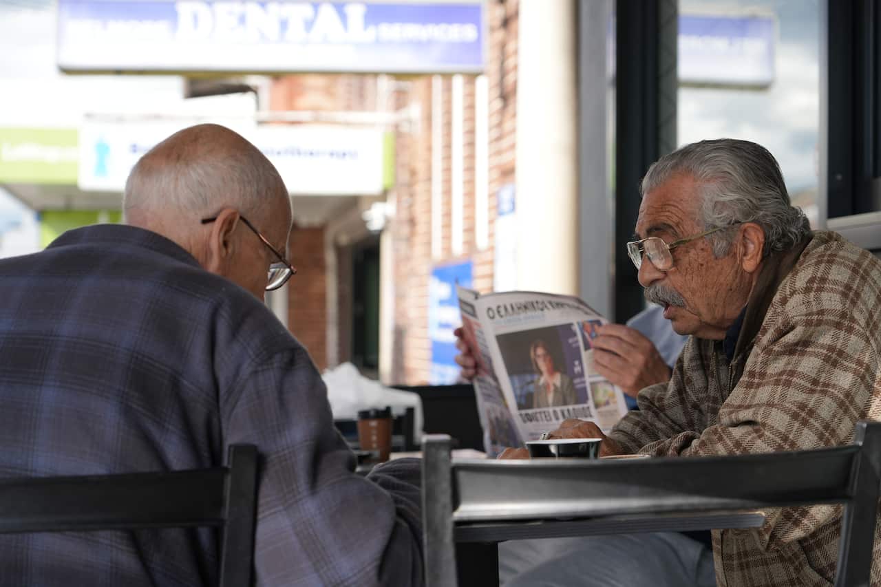The elderly men sit in a cafe reading newspapers.