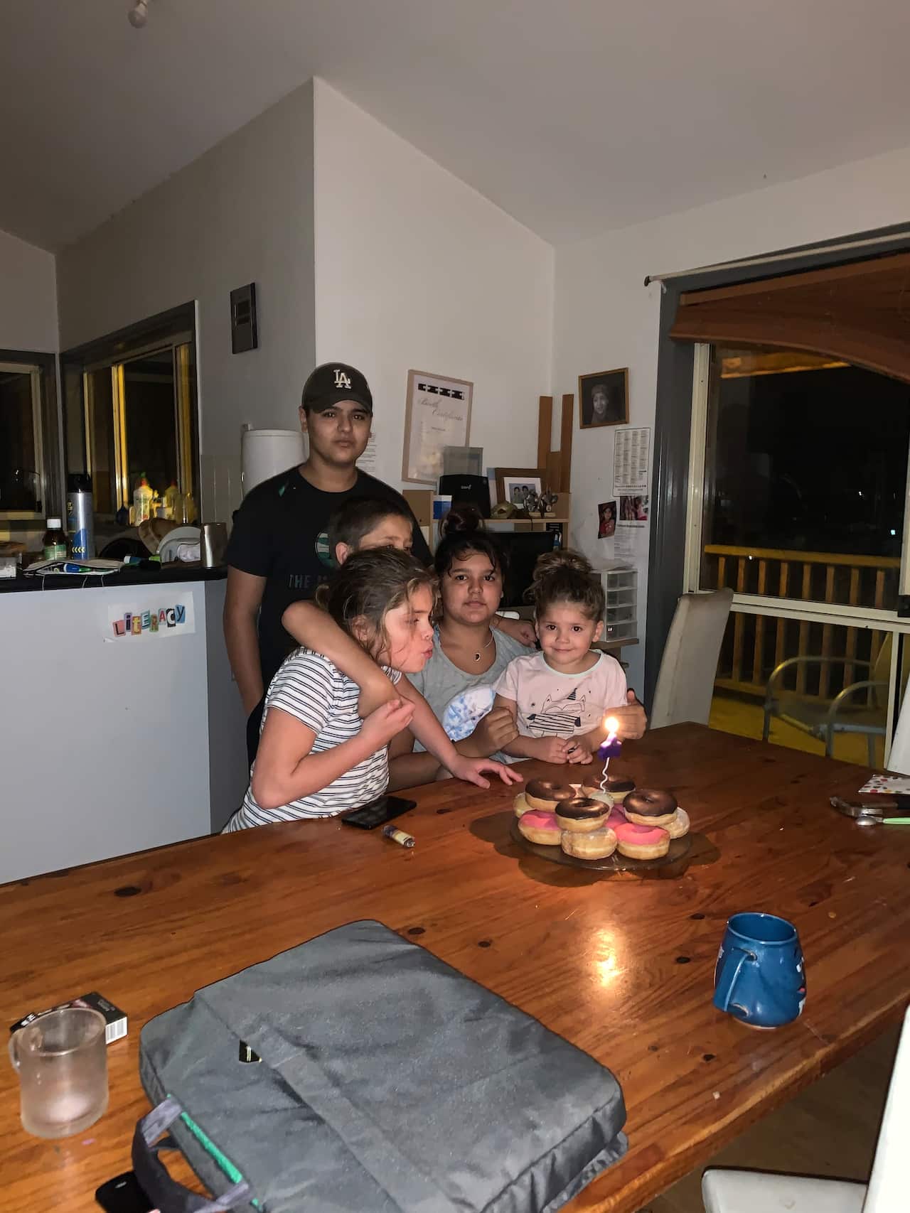 Five children sit at a table in front of donuts with a candle.