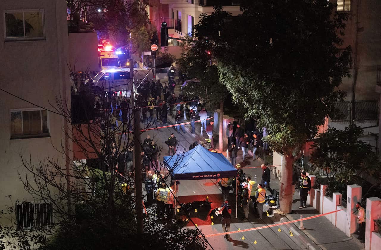 A medical emergency tent is set up on a residential street, with emergency personnel standing next to it and a crowd gathered at a distance.