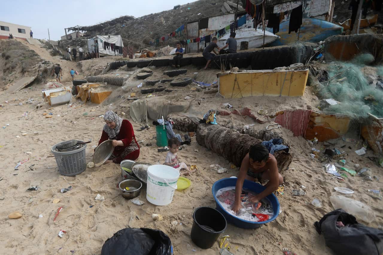 A man and a woman wash items while sitting/squatting in the sand.