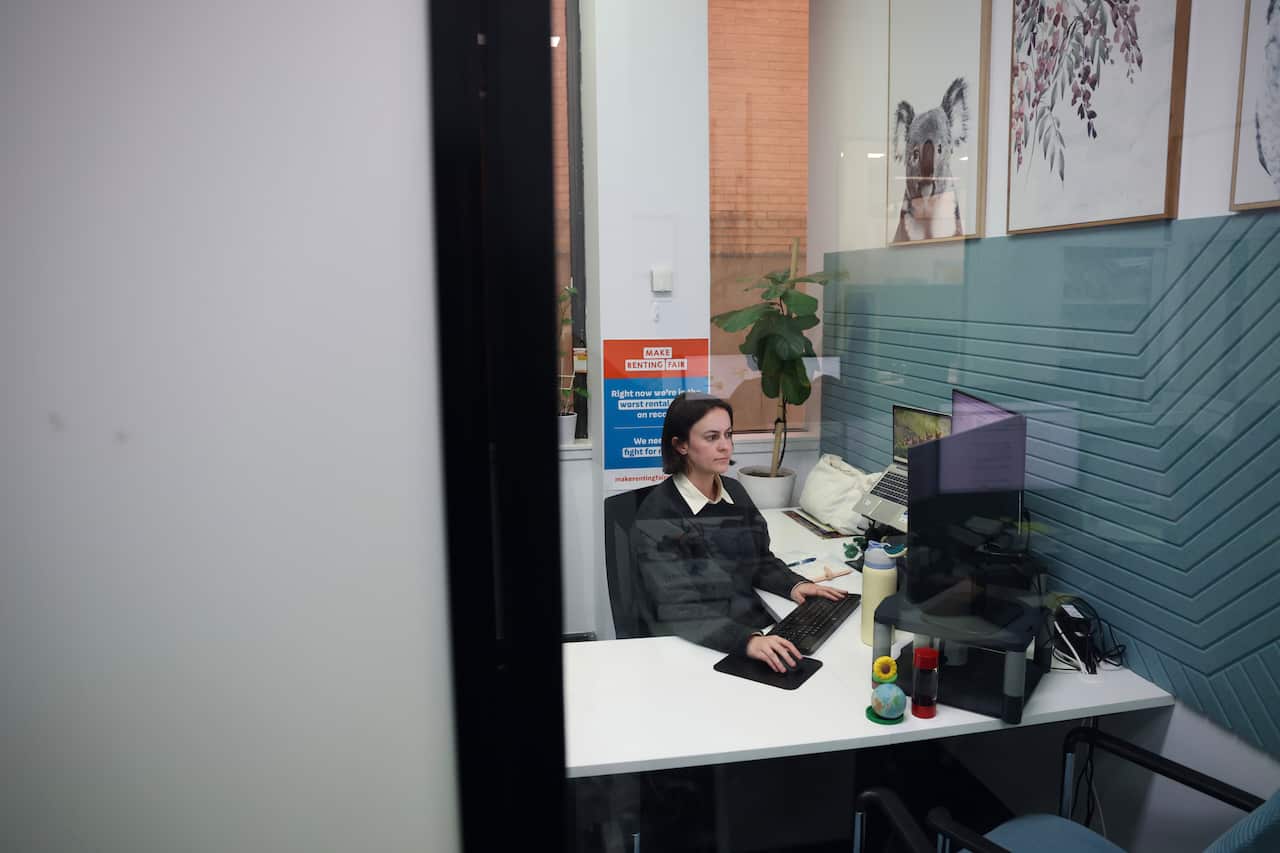 A lawyer seen through her office window, hard at work attending to administrative duties on her computer.