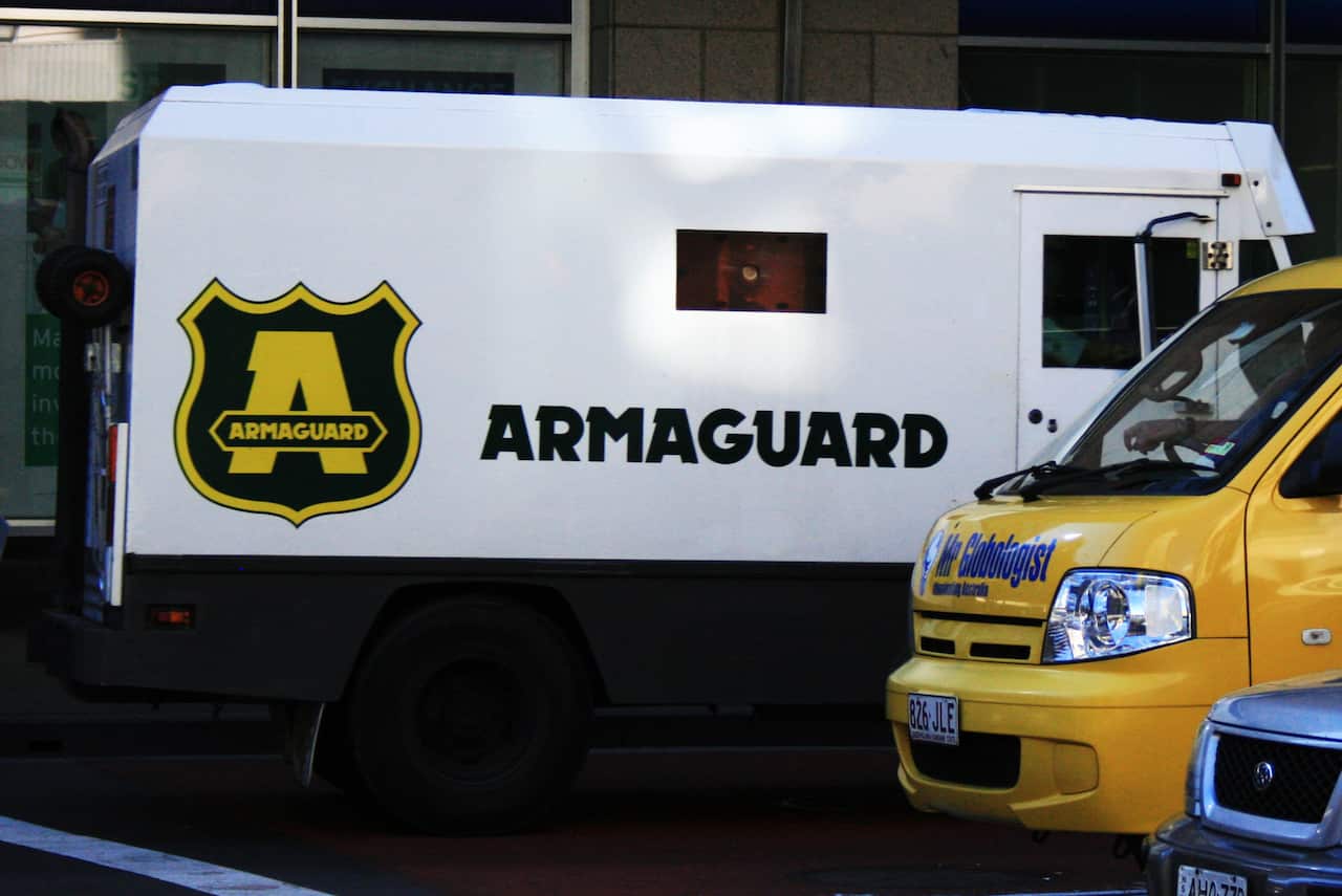 A white truck that says Armaguard on the side, next to a smaller yellow truck.