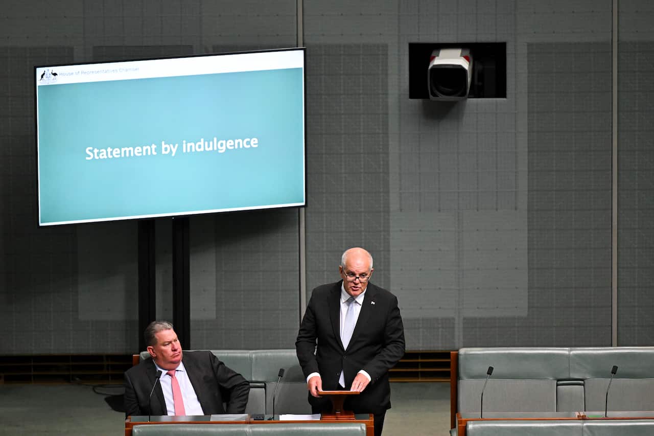Two men in suits - one seated, one standing - in parliament.