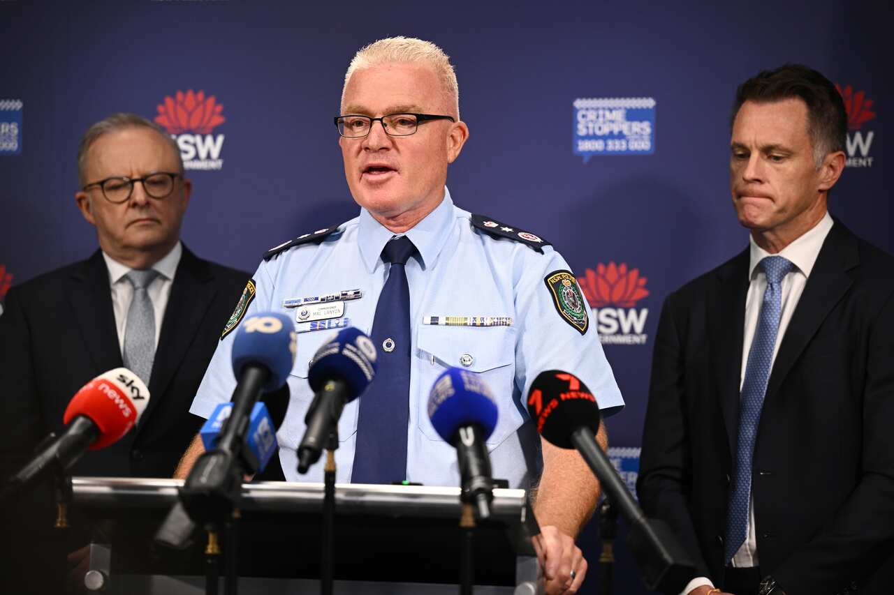 Mal Lanyon speaking at a podium in police uniform flanked by Albanese and Minns
