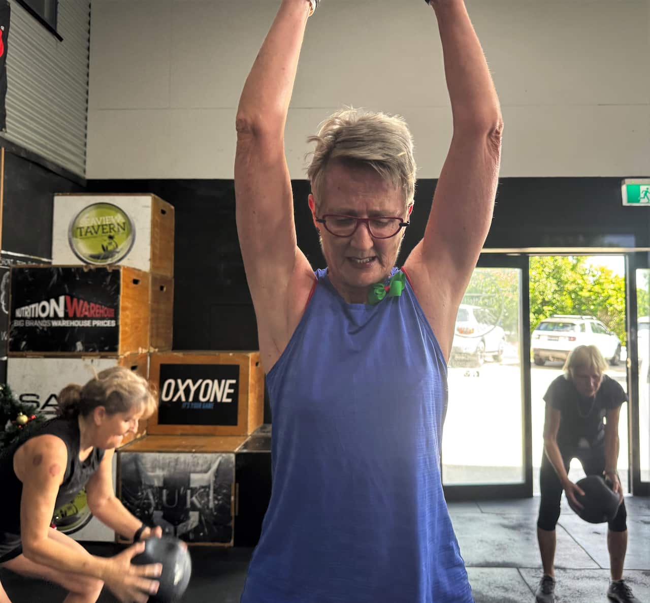 A woman in a purple singlet top raises her arms at a gym.