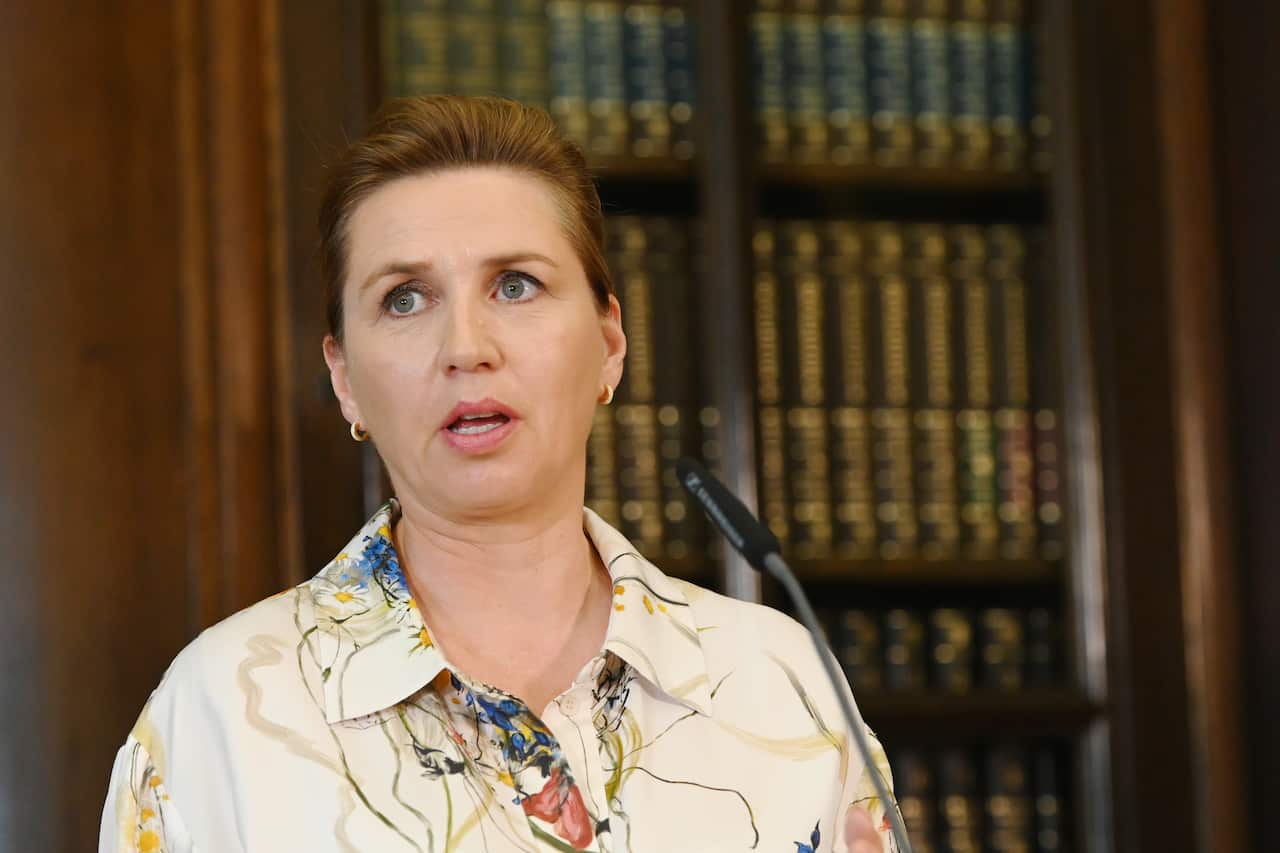 A woman speaking into a microphone in front of a cabinet containing books.