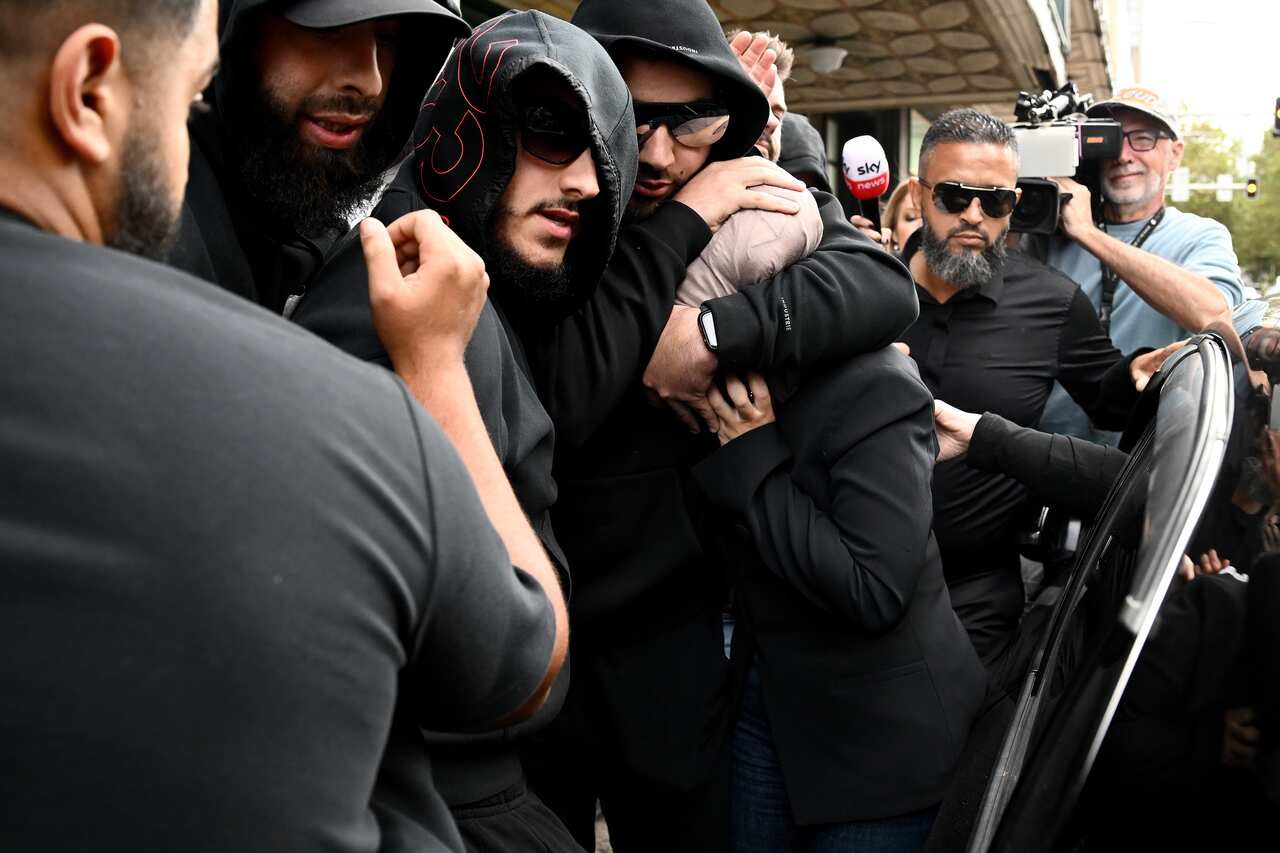 Men dressed in black surround a woman dressed in black and wearing a headscarf 