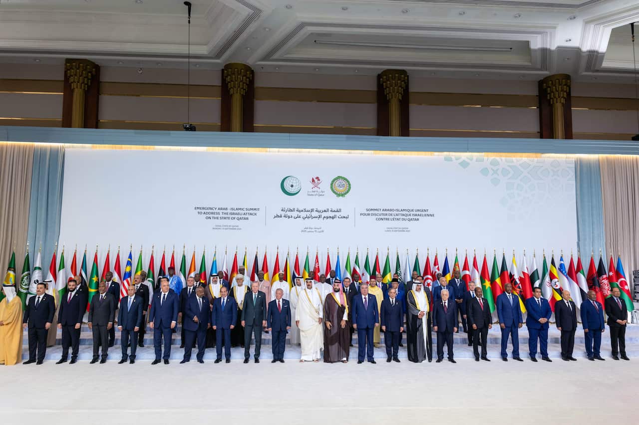 Men in suits or Arab dress standing in a line in front of a row of flags