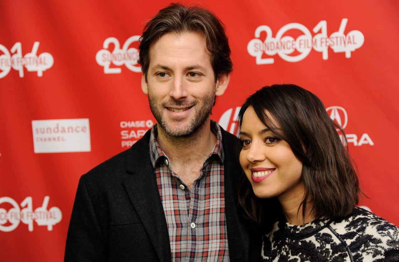 A man and a woman in front of a red backdrop with the Sundance Film Festival logo.