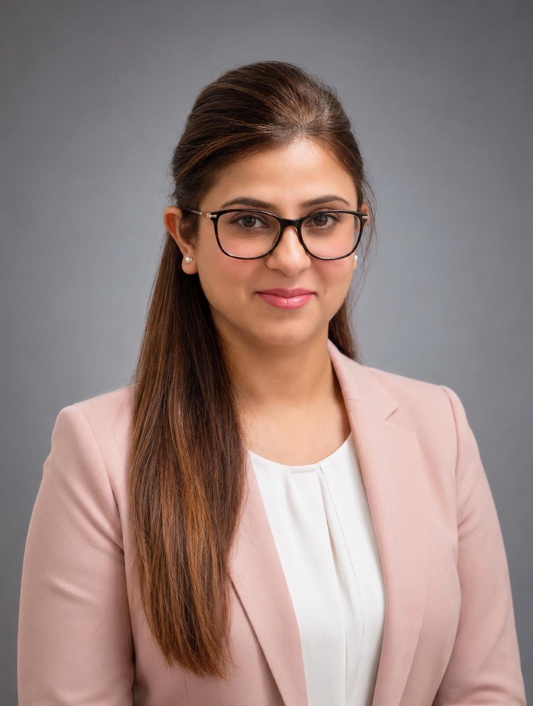 A woman with long hair, wearing a pink blazer, is smiling.