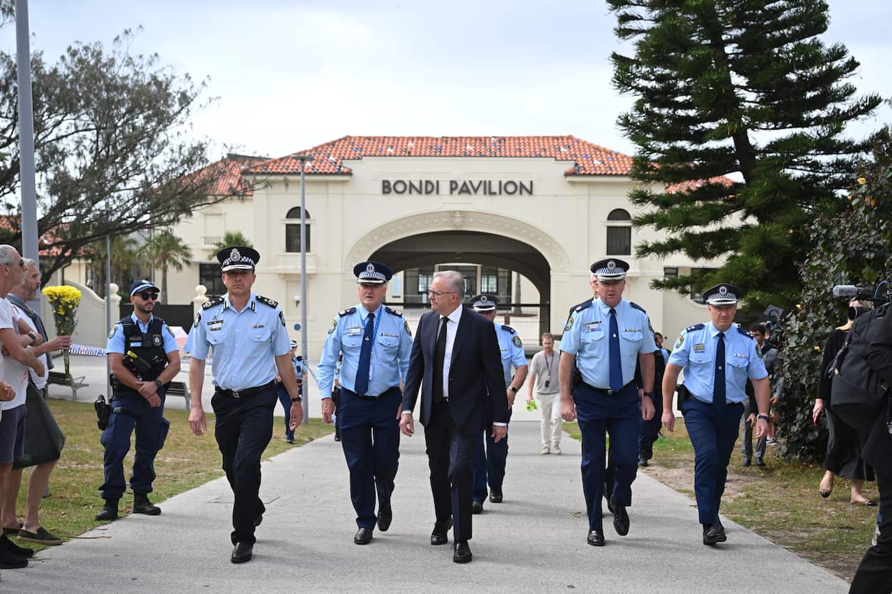 Anthony Albanese, in a black suit, walks with police officers around him.