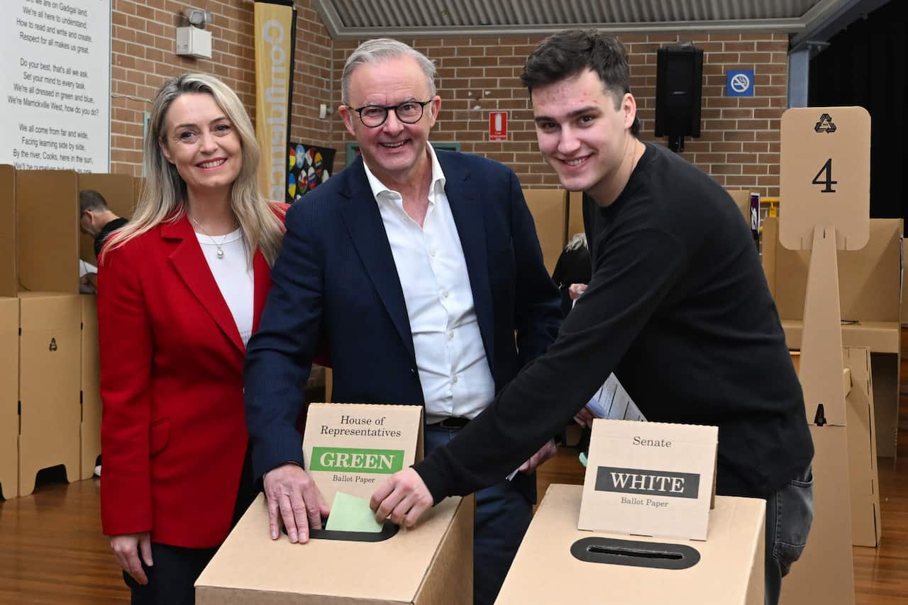 Three people smile at a voting centre while casting their votes