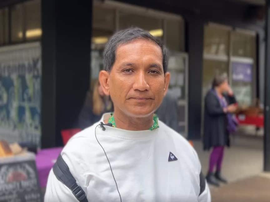 A man of Asian descent wearing a white sweater and sunflower lanyard