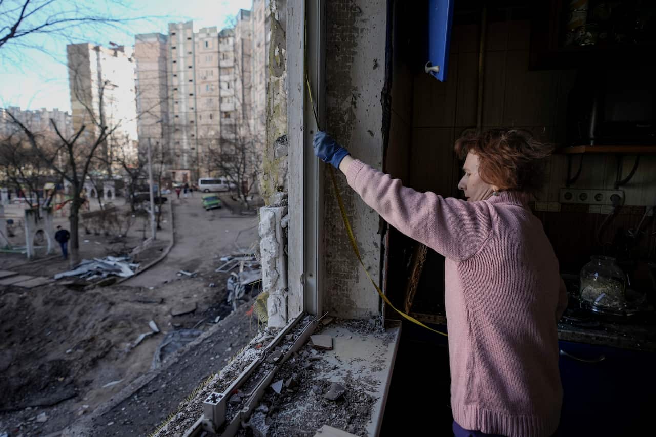 A woman is seen measuring a window that has had its glass shattered.