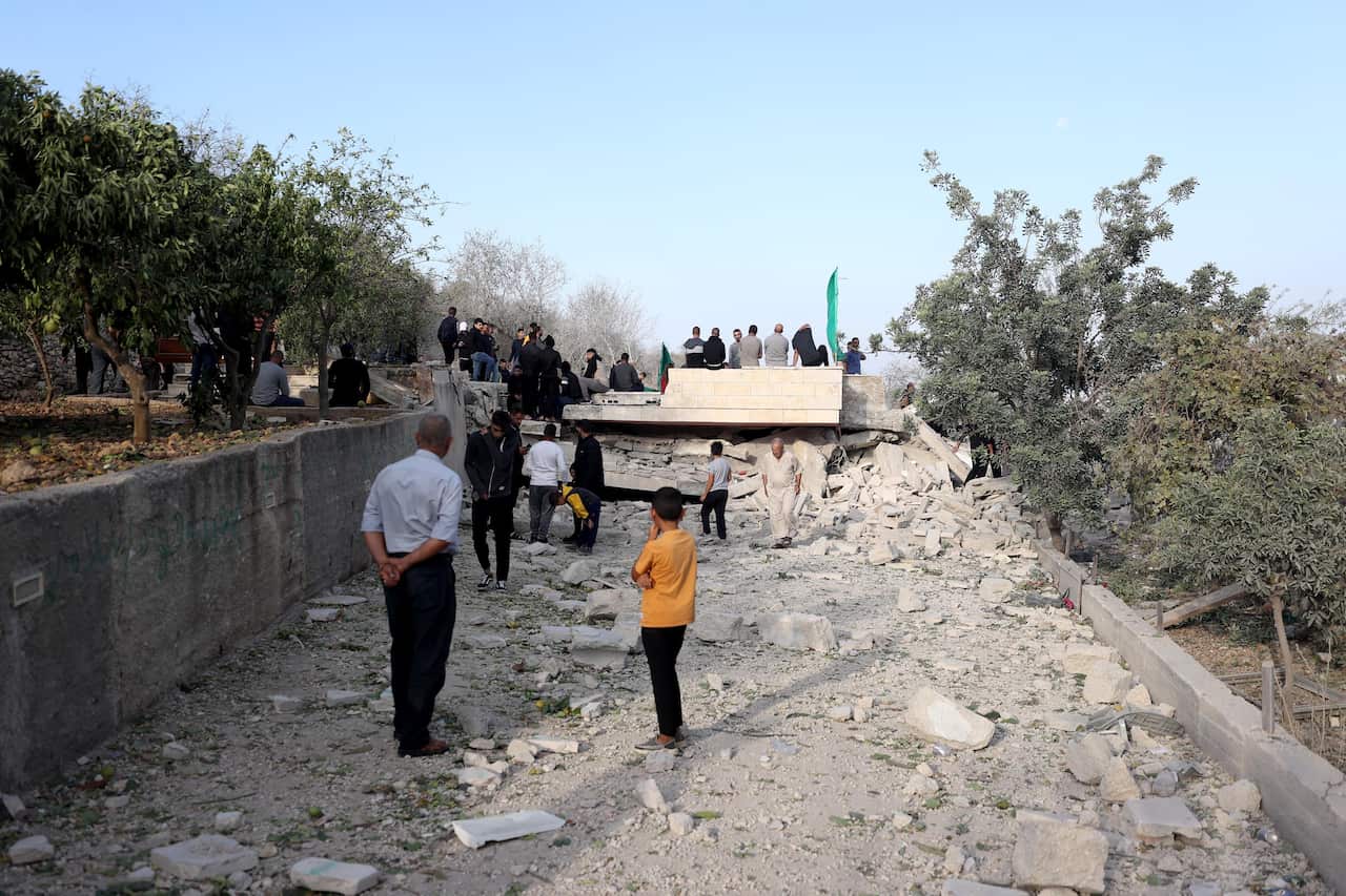A group of people standing and sitting amid the rubble of a house.