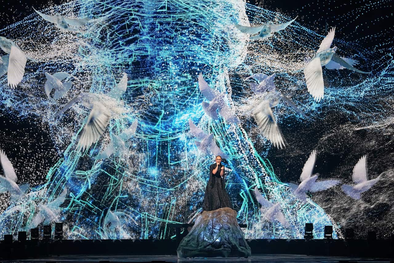 A performer on stage with a backrop of lights and images of birds