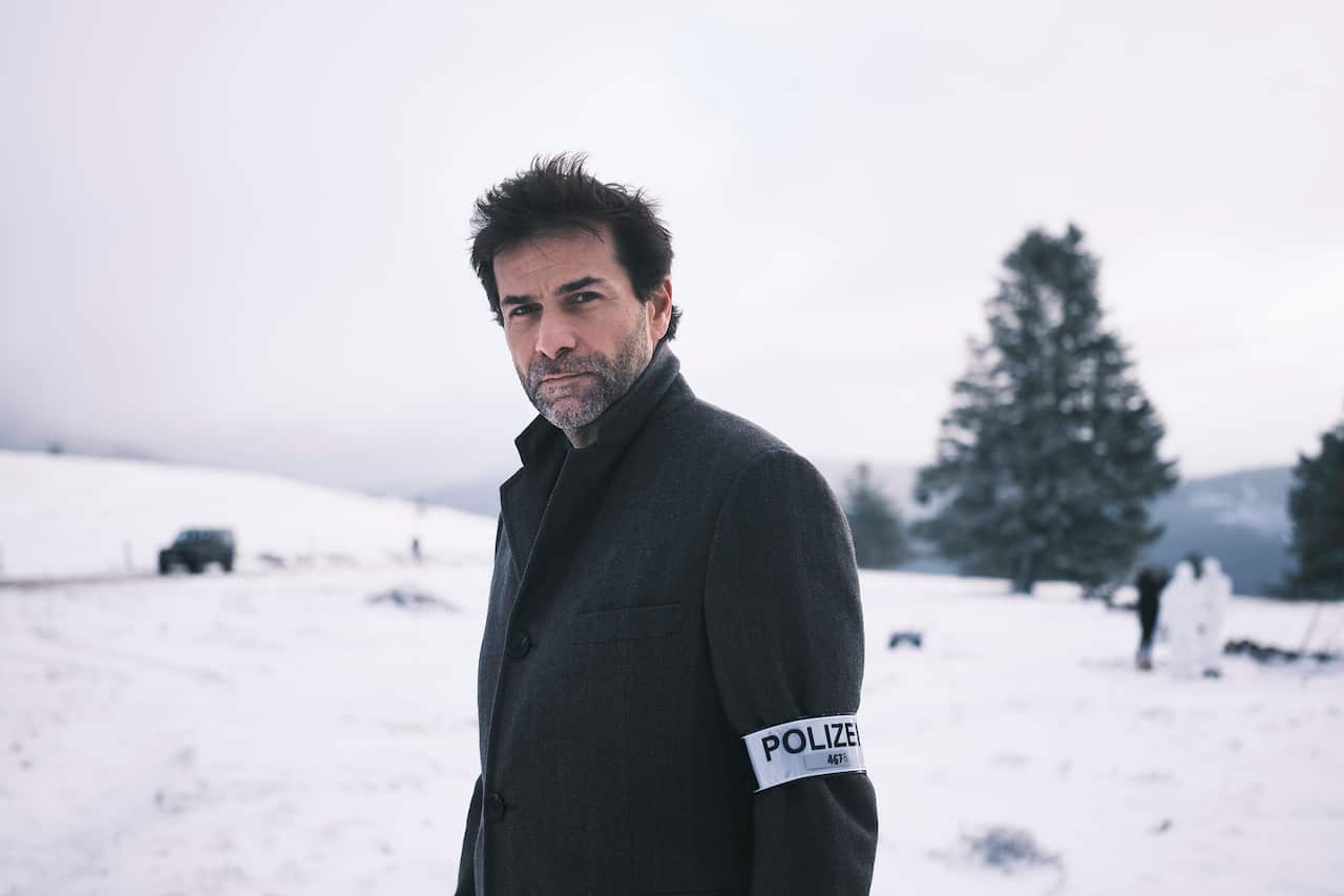 A man in a dark coat stands in a snowy landscape. 