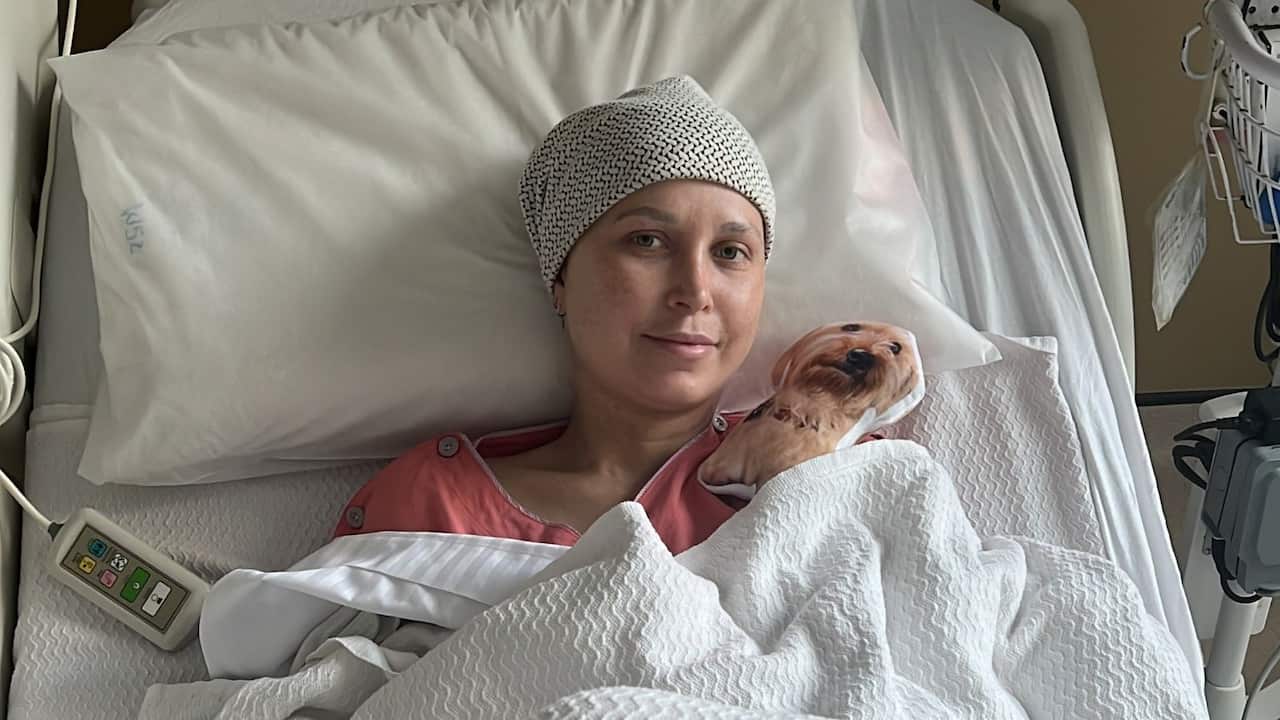 A young woman wearing a beanie lies in a hospital bed