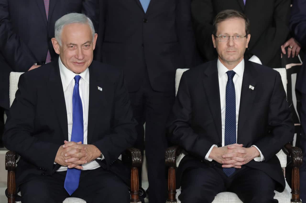 Two men in suits and ties sit with folded hands.