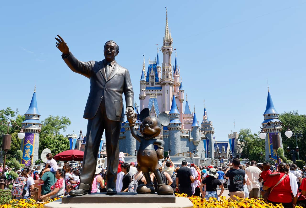 A statue of a man with a cartoon mouse with a large crowd around it and a castle visible in the background