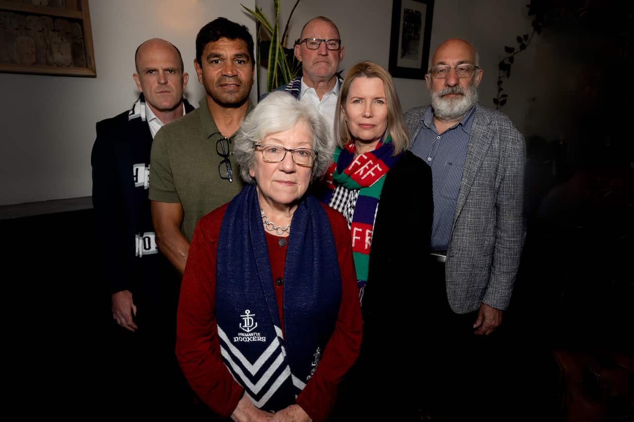 Group of six people standing together wearing Fremantle Dockers scarves.