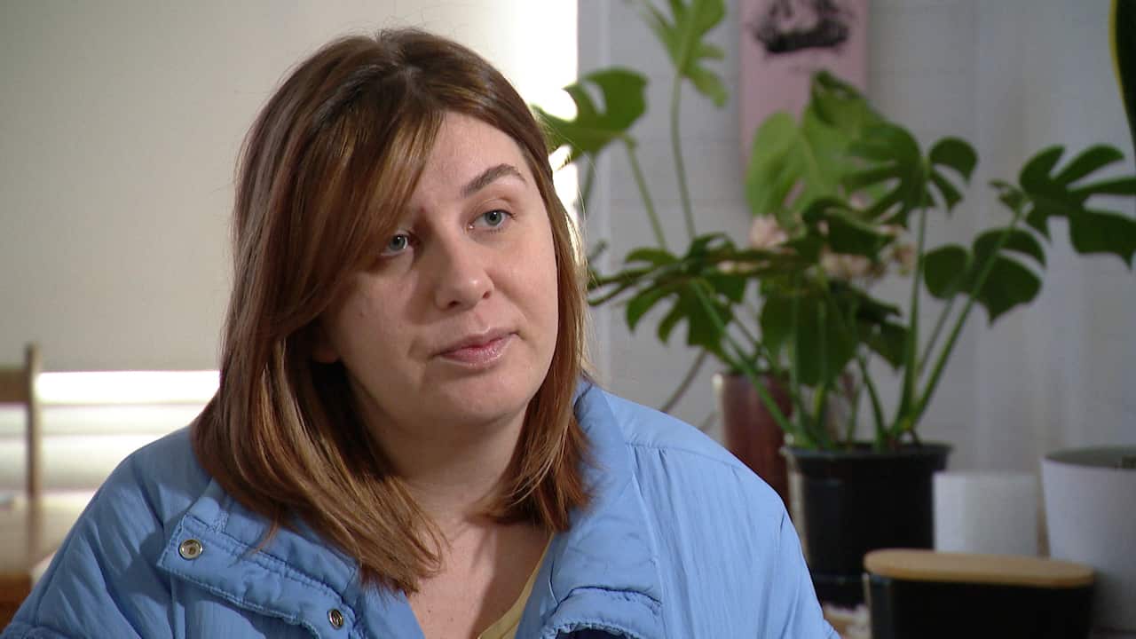 A woman in a blue puffer jacket sitting down. Some indoor plants are in the background.