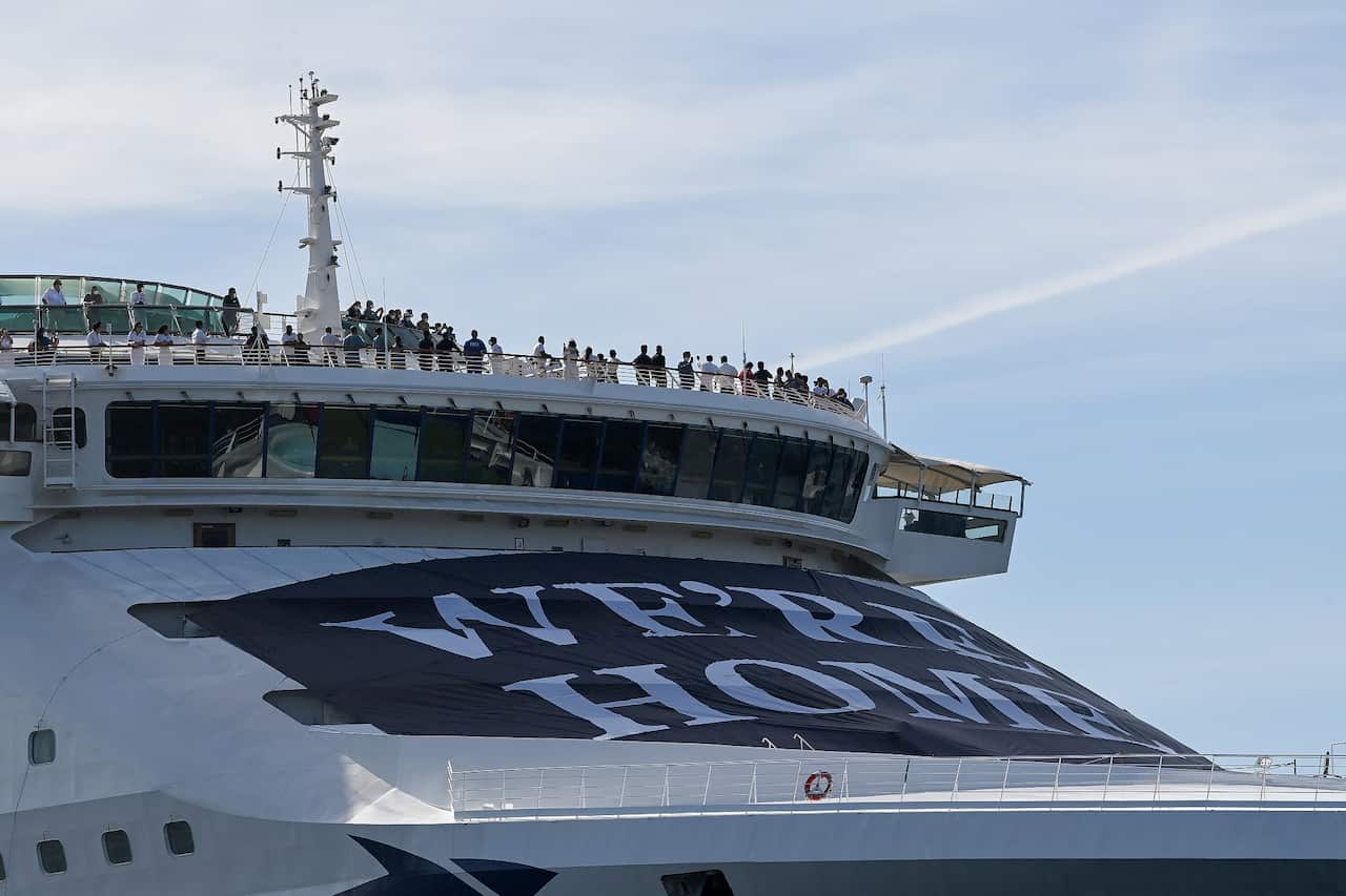 Crew members are seen above a ‘We’re Home’ banner onboard the P&O Cruises Australia flagship Pacific Explorer as it enters the Sydney Harbour. 