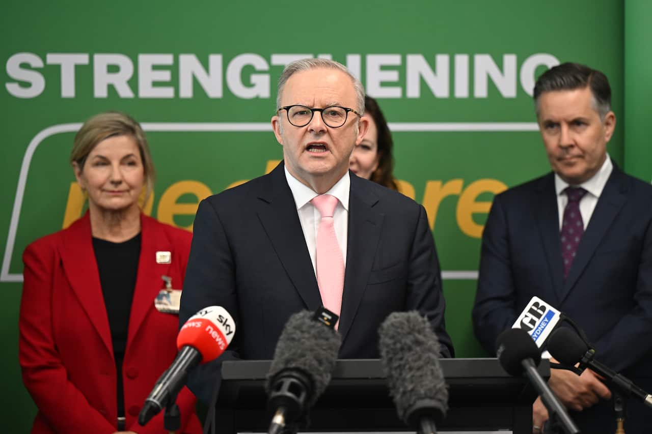 Anthony Albanese speaks to the media with people in suits behind him.