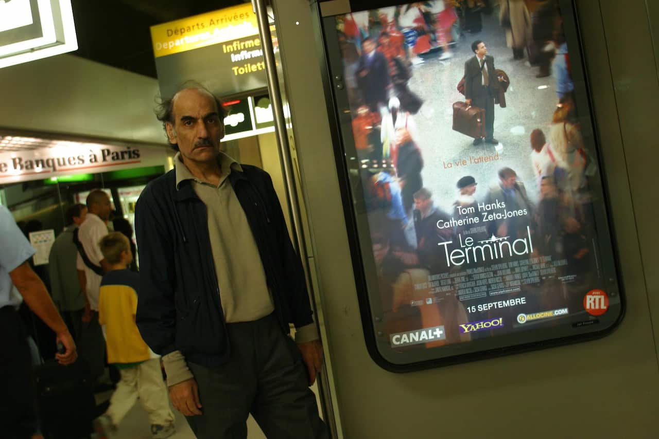 Mehran Karimi Nasseri stands in front of a poster of Steven Spielberg's movie 'The Terminal', which was loosely based on his life in Charles de Gaulle Airport Terminal 1.