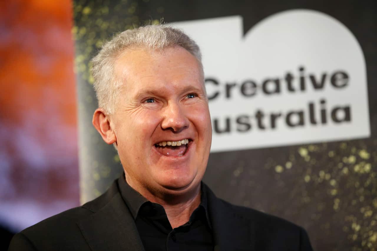 A man with short grey hair smiling broadly, in front of a banner that reads "Creative Australia".
