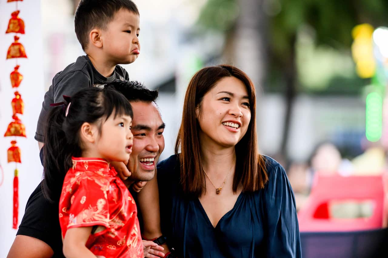 A family of four, including a child in a bright red top, pose together, in front of a bright, out-of-focus background.