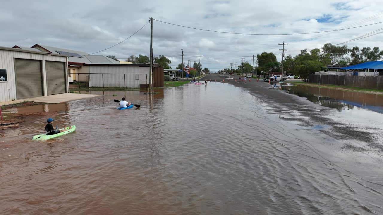 Kids in kayaks float down a flooded residential street. 
