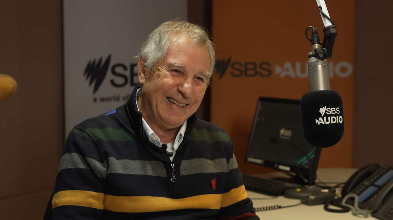 A journalist sitting in a studio. In front of him is a microphone that says "SBS Audio". 