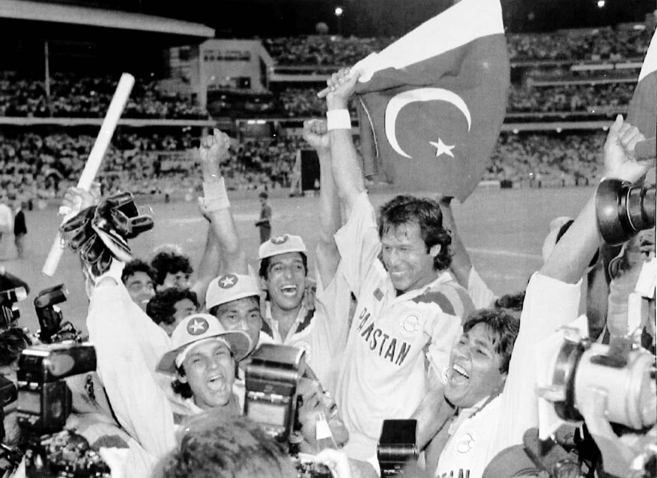 Greyscale photo of former Pakistan cricket captain Imran Khan waving a flag an celebrating with teammates.