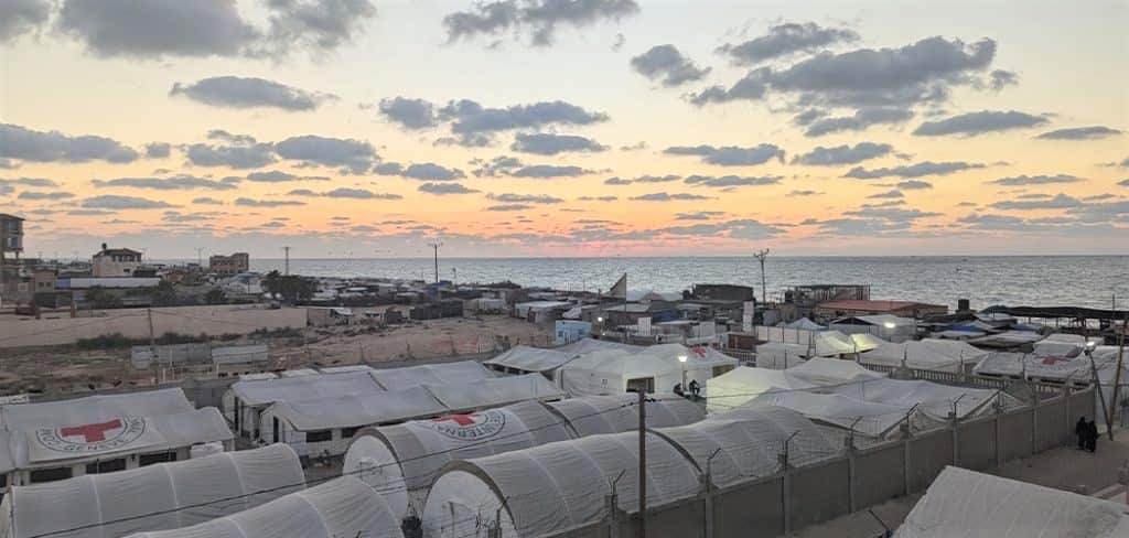 A series of curved makeshift tents lined up in a campsite beside the ocean.
