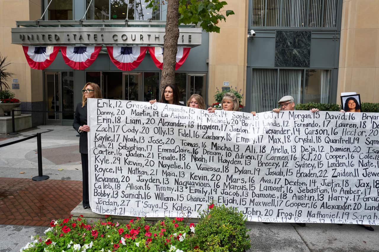 A group of protesters holding signs addressing youth mental health and social media safety outside a building entrance.