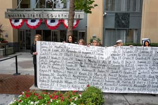 A group of protesters holding signs addressing youth mental health and social media safety outside a building entrance.