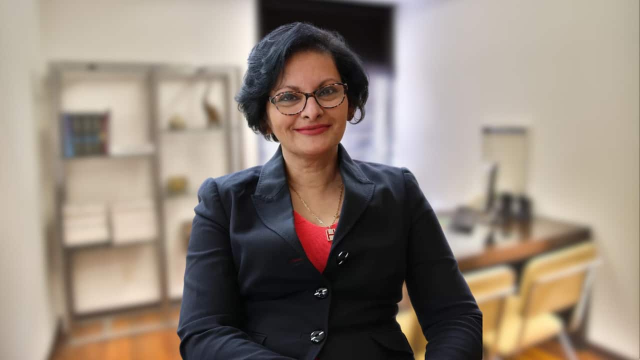 A woman with short dark hair and glasses smiling as she poses for a photo.