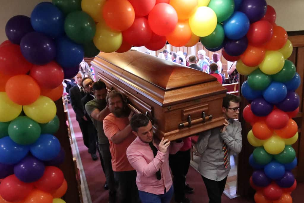 Pallbearers carry a coffin under an arch of balloons.