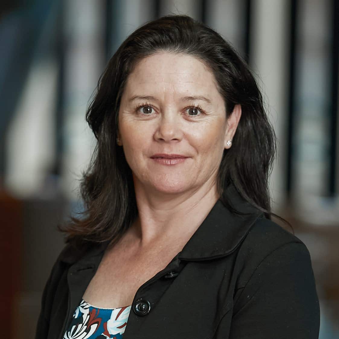 A woman with dark hair, wearing a patterned top and black jacket