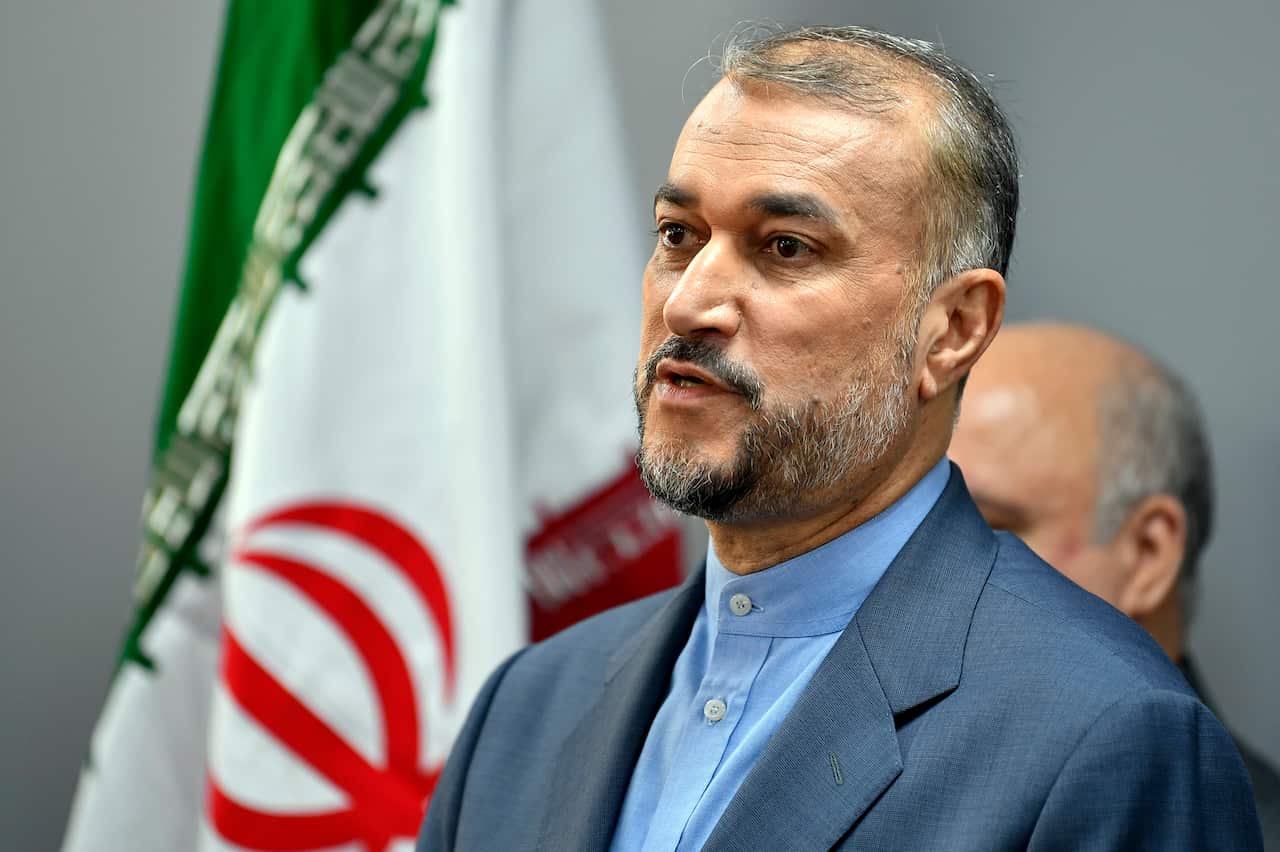 A man wearing a suit inside. Iran's flag is in the background.