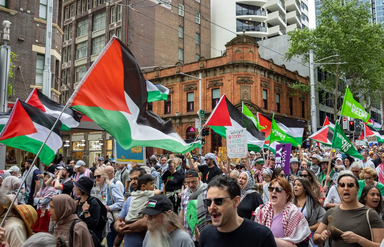 A large crowd of people waving Palestine flags walks through a street in Sydney's CBD