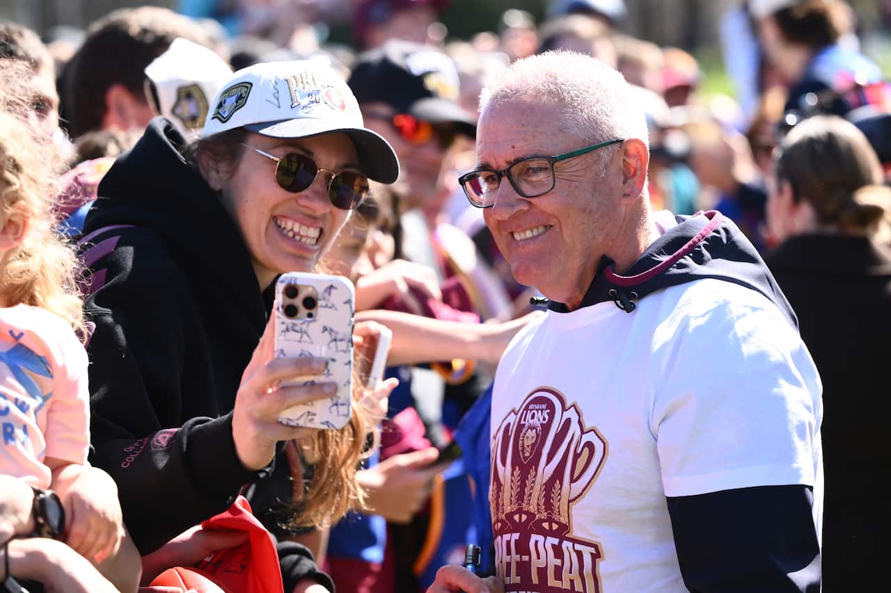 A man smiles and poses for a selfie with a woman in a crowd.