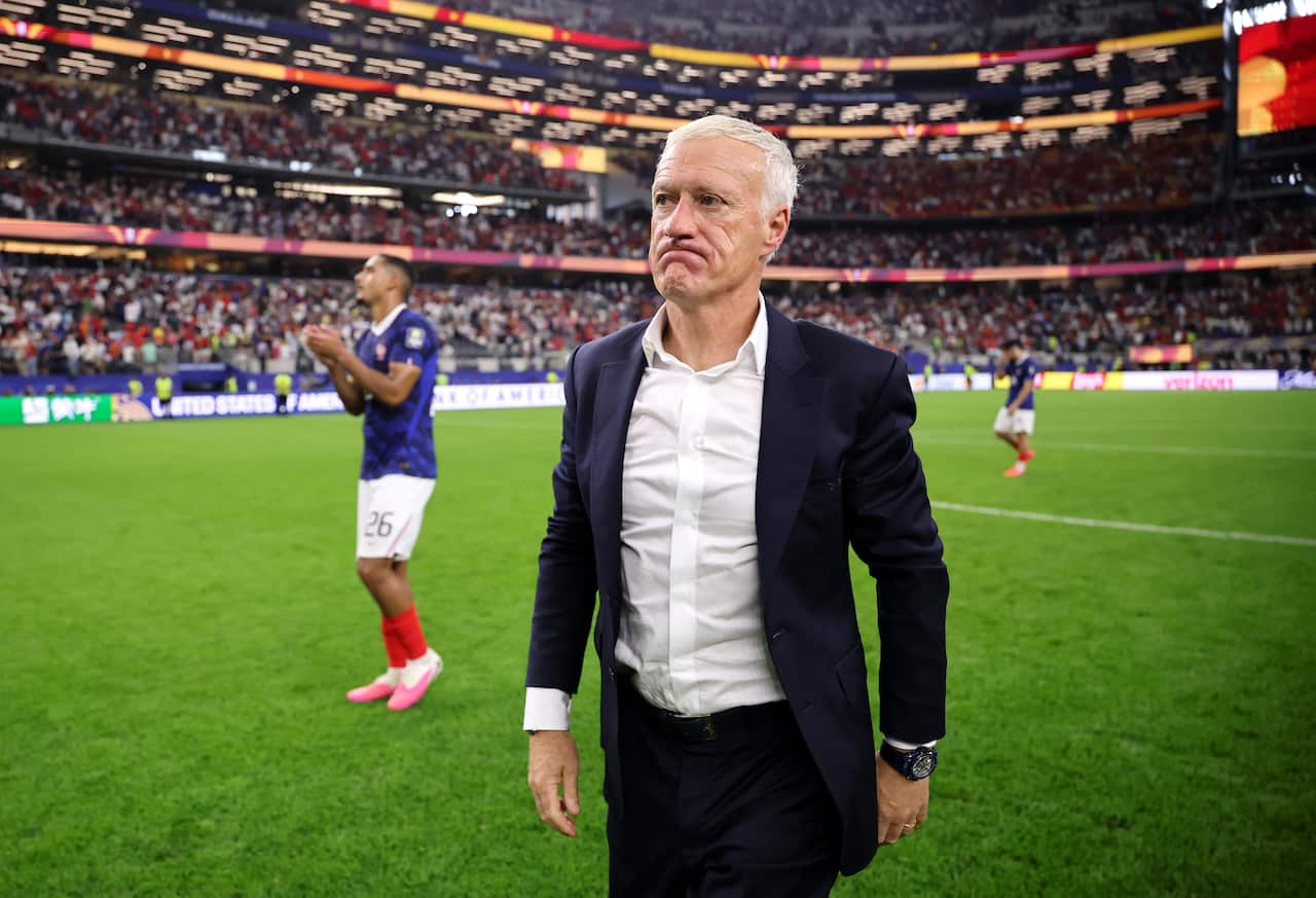 A middle-aged white man in a suit frowning as he walks off a football pitch