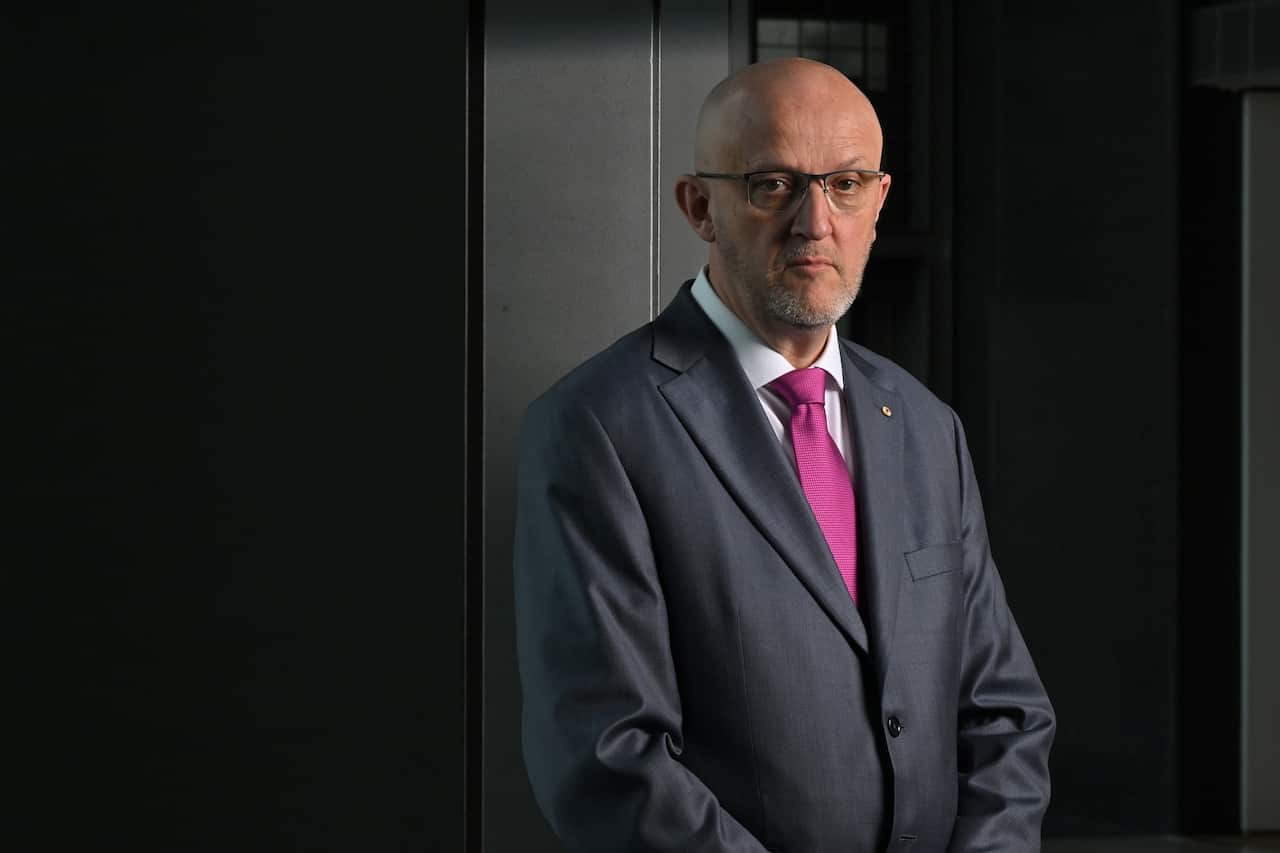 A man in a grey suit and pink tie poses for a photo