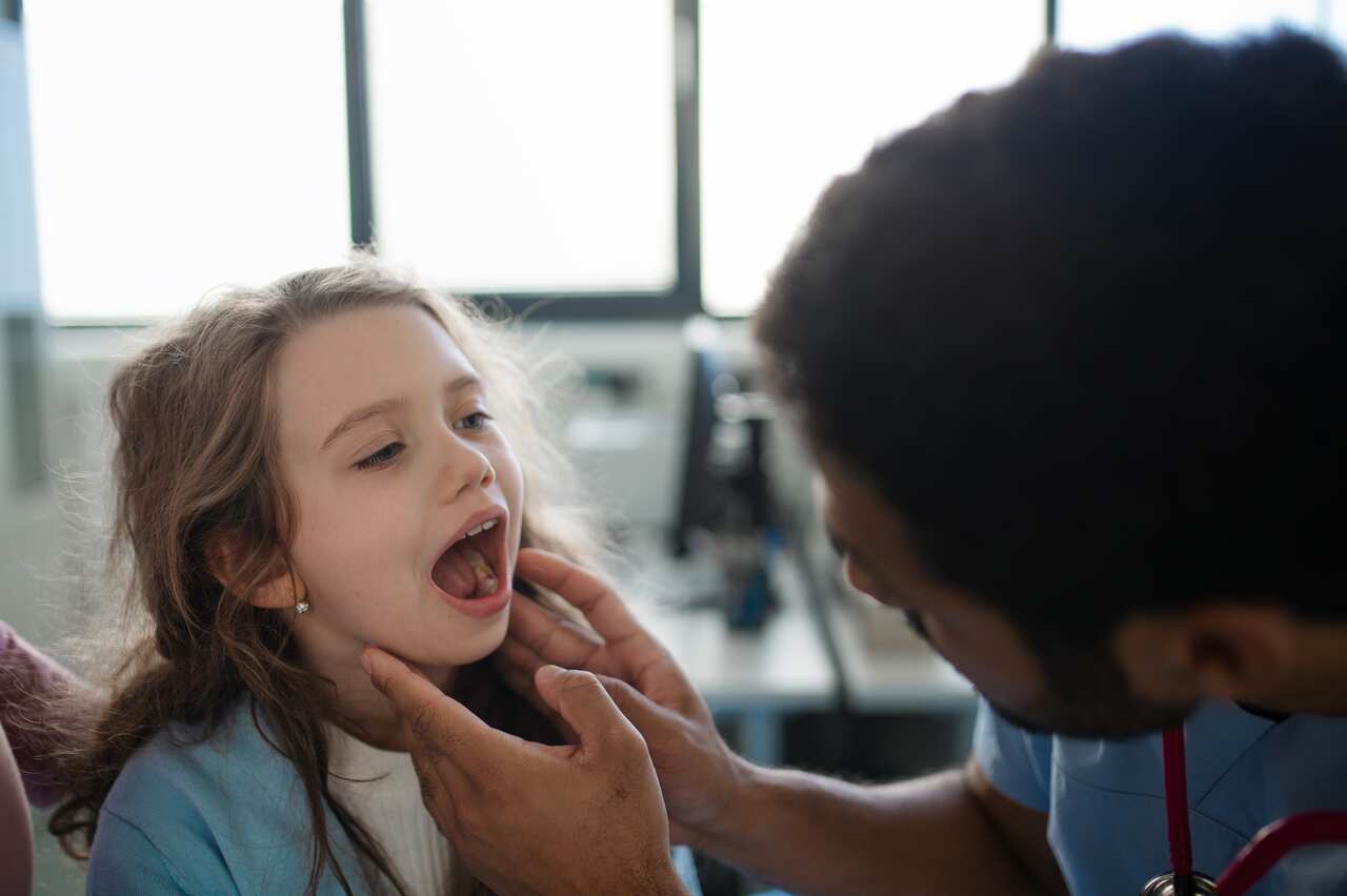 A young girl opening her mouth for a doctor to examine her.